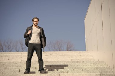 Mavi gökyüzü arkaplanına karşı basamaklarda oturan düşünceli genç adam