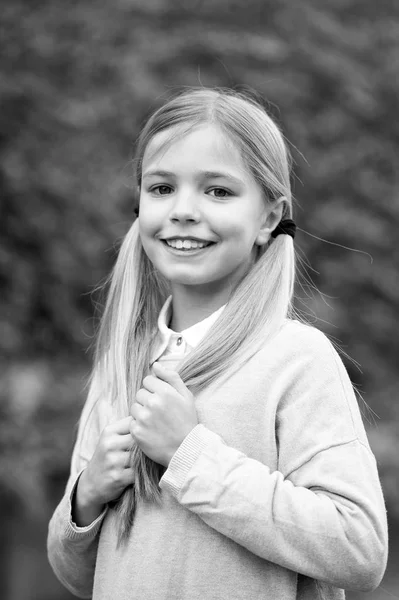 Penteado e conceito de cuidado do cabelo. Menina no rosto sorridente posando com duas caudas, fundo natural verde. Menina gosta de olhar bonito, elegante e elegante. Menina criança com cabelos longos parece adorável — Fotografia de Stock