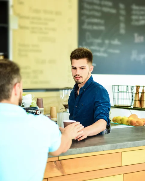 Enjoy your drink. Barista handsome stylish hipster communicate with client visitor. Barista at bar of modern cafe ready serve coffee for client. Served coffee to go. Man ask for drink at bar counter