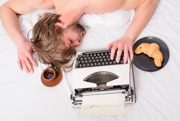 Spisovatel používá staré staromódní psací stroj. Ospalý muž ležel lůžkoviny při práci. Workoholik usnout. Při pohledu shora psát kapitola usnete autor rozcuchané vlasy. Posteli ležel muž s psacím strojem káva — Stock fotografie