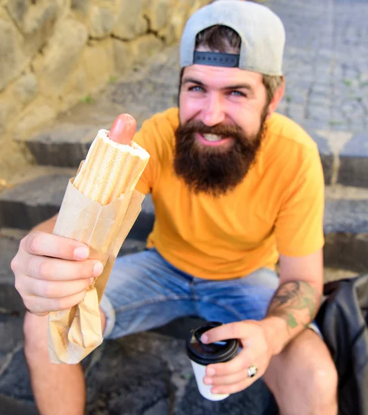 Conceito de cultura alimentar urbana. Hipster comer cachorro-quente enquanto se sentar em escadas ao ar livre. Aproveite o seu conceito de refeição. Homem hipster barbudo desfrutar de comida de rua fundo urbano. Salsicha de cachorro-quente saborosa em pão torrado — Fotografia de Stock