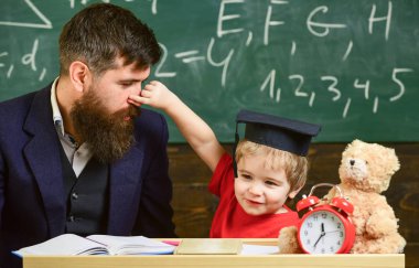 Baba sakallı, evlat, öğretmen öğretir burnunu pinching çocuk iken küçük çocuk. Neşeli oyun baba ile çocuk. Oynak çocuk kavramı. Öğretmen ve öğrenci kolej, kara tahta arka plan içinde