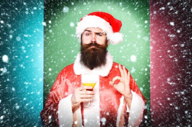 Yakışıklı, sakallı, uzun sakallı, ciddi sakallı Noel Baba elinde bir bardak alkollü içecek ya da Noel süveteri ve renkli stüdyo geçmişinde onaylanmış yeni yıl şapkası tutan adam.