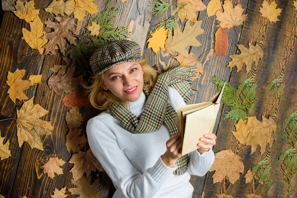 She likes detective genre. Girl blonde lay wooden background with leaves. Woman lady in checkered hat and scarf read book. Girl in vintage outfit enjoy literature. What to read in autumn book list