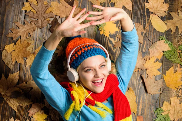 Fall cozy atmosphere. Fall and autumn season. Girl cheerful face listen music lay on wooden background with leaves top view. Autumn melody concept. Woman knitted hat and scarf listen music headphones