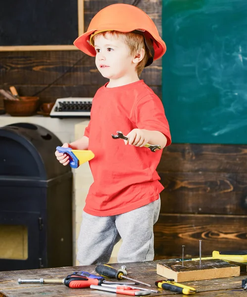 Yan görünümü çocuk atölyede ayakta. Sarışın çocuk tutan somun anahtarı ve el testeresi turuncu kask içinde. Küçük tamirci resim için poz — Stok fotoğraf