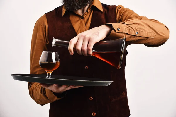 Barman in vintage suede leather waistcoat pours scotch or brandy.