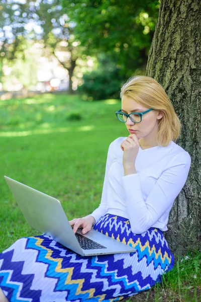 Nő laptop működik szabadtéri, park háttérrel. Lány ül fű sovány fa törzse notebook. Wi-fi hálózati kapcsolat ingyenes hozzáférés. Szörfözés internet a természetben. Lady szabadúszóként dolgozik park — Stock Fotó