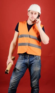 Mühendis, mimar, Smartphone cep telefonu ile ayrı tutma planları süre meşgul yüzünde konuşuyor. Adam, konuşan, kırmızı arka plan kask içinde foreman. Planı düzeltmek için arama mühendis mimar. İletişim kavramı