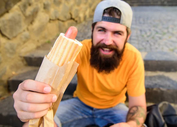 Tasty hot dog sausage in roasty bun. Fast snack nutrition value. Urban food culture concept. Hipster eat hot dog while sit on stairs outdoors. Man bearded hipster enjoy street food urban background