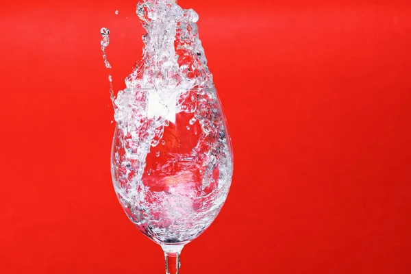 Spruzzata d'acqua in bicchiere di vino su sfondo rosso, copiare lo spazio . — Foto Stock