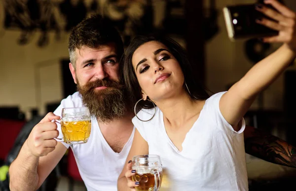 Couple in love on date drinks beer. Man bearded hipster and girl with beer glass full of craft beer. Best friends or lovers drinking beer in pub. Take selfie photo to remember great date in pub