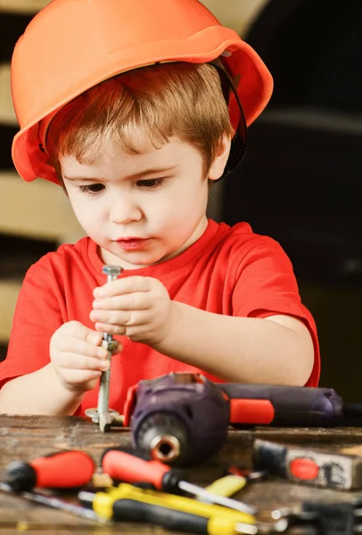 儿童在硬帽, 头盔发挥与六角螺栓作为建设者或修理工, 就要手工制作。幼儿在繁忙的脸上玩螺栓在家里的车间。小男孩扮演杂工。就要手工制作理念 — 图库照片