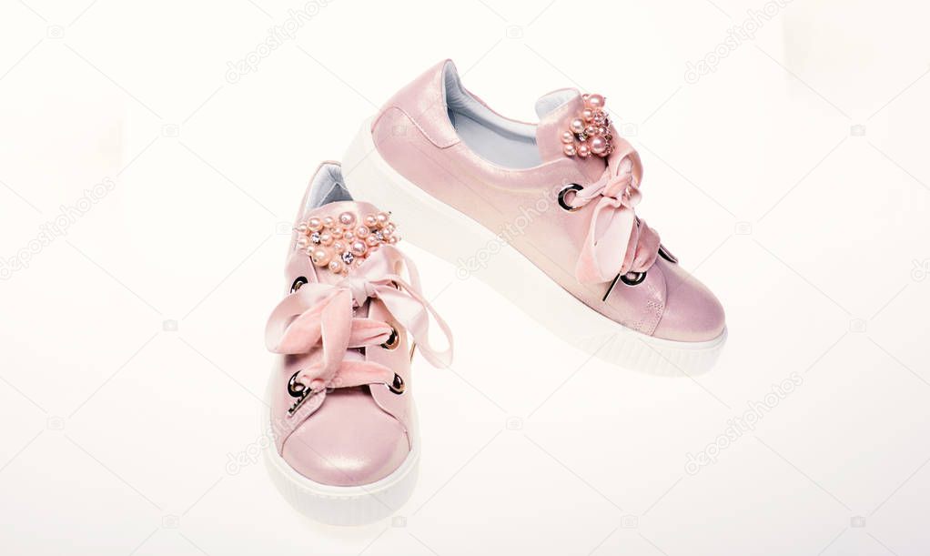 Glamorous sneakers concept. Footwear for girls and women decorated with pearl beads. Pair of pale pink female sneakers with velvet ribbons. Pink glamorous womens sneakers isolated on white background