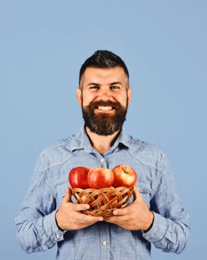 Sakallı adam elinde meyve dolu hasır kasesi tutuyor.