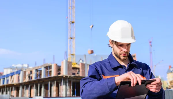 Casque de protection ingénieur debout en face de fond bleu ciel. Contrôle de l'entrepreneur selon le plan. Constructeur ingénieur casque travaille sur le chantier de construction. Contremaître processus de construction de contrôle — Photo