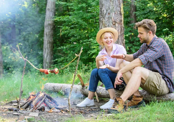 Couple tourists throwing their gesture while sit log near bonfire. Hand gesture game decide who win. Winner eats first. Man and girl play hand gesture game. Couple play rock paper scissors hand game