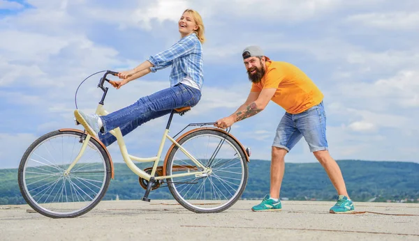 Learn cycling with support. Woman rides bicycle sky background. Man helps keep balance and ride bike. How to learn to ride bike as adult. Girl cycling while boyfriend support her. Cycling technique