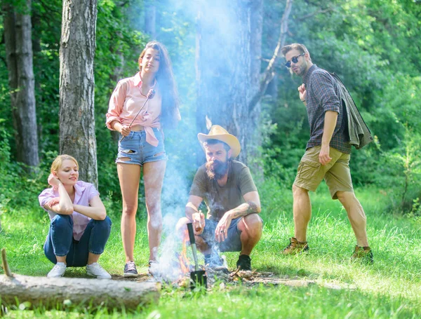 Amici incontro a prato per appendere fuori e preparare salsicce arrosto snack sfondo natura. La compagnia si diverte mentre arrostisce salsicce su bastoncini. Ci riuniamo per un bel picnic. Iscriviti picnic estivo — Foto Stock