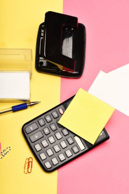 Office stationery and calculator on yellow and pink background clipart