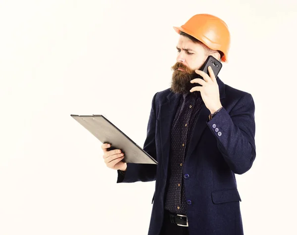 Homem barbudo usa capacete de construção. Empreendedor detém plano de construção e fala por telefone. Arquiteto com papéis e rosto sério detém smartphone. Arquitetura, sucesso, conceito de novas tecnologias — Fotografia de Stock