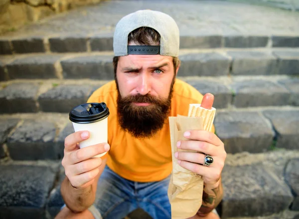 Hipster desfrutar de cachorro-quente e beber bebida copo de papel. Fast food para almoço ideia comum. Homem barbudo desfrutar rua comida escadas fundo. Hipster come cachorro-quente e bebe café. Conceito de hora de almoço — Fotografia de Stock