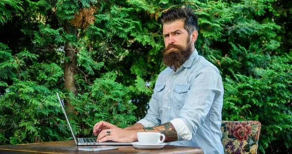 Hipster work online blog with notebook. Blogger create post while enjoy coffee. Man bearded manager entrepreneur sit terrace outdoors with laptop and cup of coffee. Create content for web blog