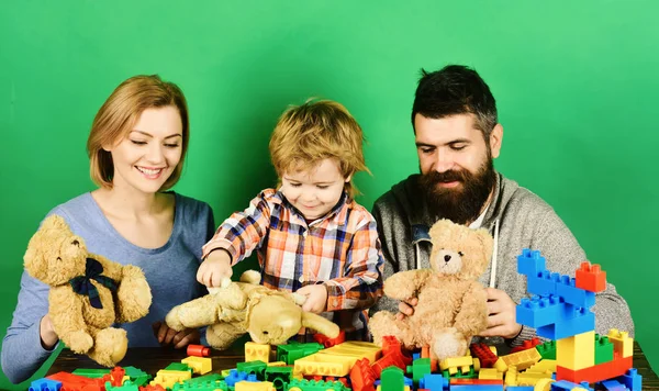 Family with curious faces hold teddy bears near construction blocks.
