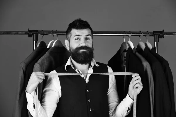 Man with beard by clothes rack. Tailor with happy face