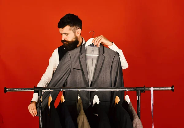 Man with beard by clothes rack. Tailor with busy face