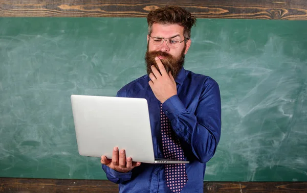 Concepto de educación a distancia. Profesor barbudo hombre con portátil moderno navegar fondo pizarra de Internet. Navegar por Internet. Hipster profesor usar gafas y corbata sostiene portátil navegar por Internet —  Fotos de Stock