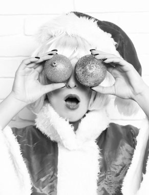 Hoş, seksi Noel Baba kız ya da sürpriz esmer kadın. Kırmızı kazak ve pembe peruklu Noel şapkalı. Beyaz tuğlalı duvarda renkli toplar, kavramsal portre..