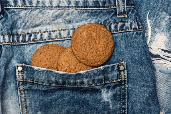 Biscoitos de aveia no bolso das calças. Biscoitos em fundo tecido jeans azul. Doce padaria e lanche. Refeição para ir conceito — Fotografia de Stock