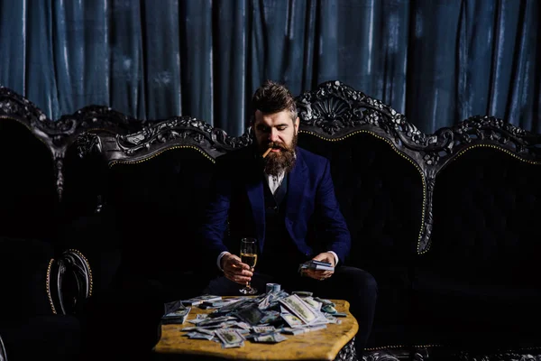 El joven rico sosteniendo un vaso de whisky y un montón de dólares en la mesa . — Foto de Stock