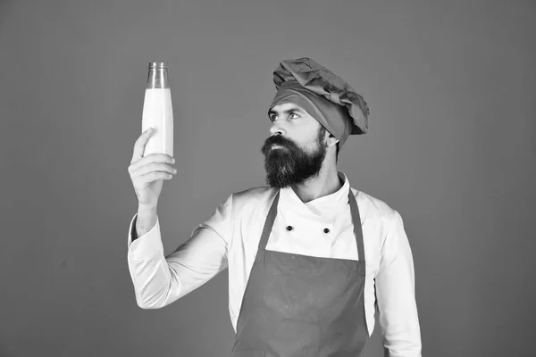 Cook med nyfiken ansikte i vinrött uniform håller mjölk. — Stockfoto