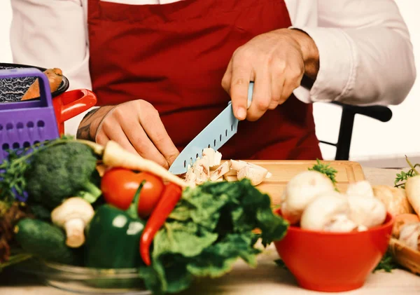 Cook burgundy uniform cuts vegetables. Male hands cut mushroom