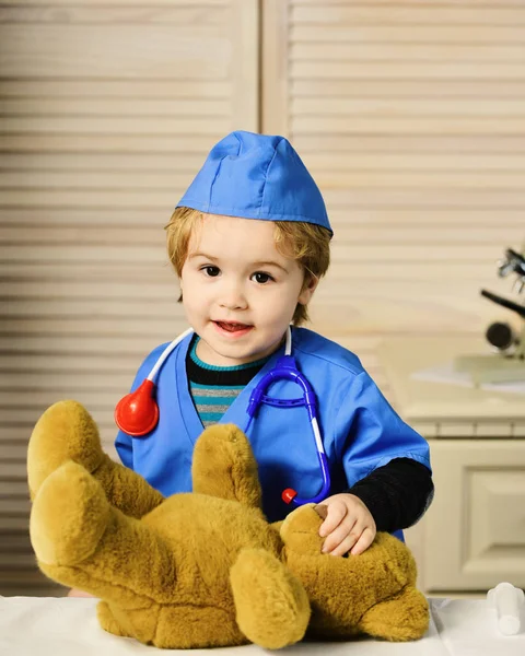Kid in doctor coat plays with teddy bear — Stock Photo, Image