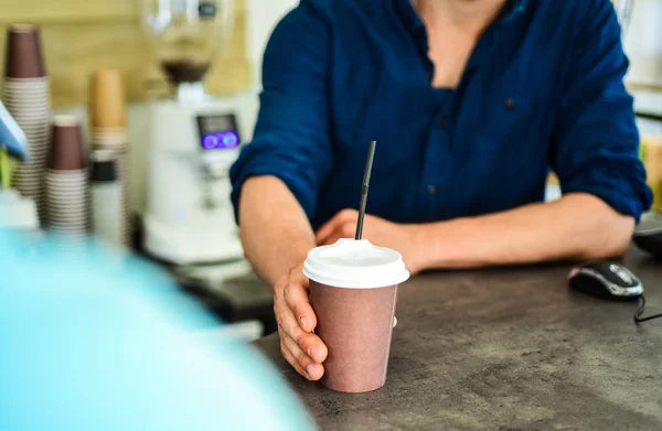 Hand gives cup to client visitor. Man receive drink at bar counter. Cappuccino or cacao with straw. Served in paper cup coffee to go. Hand of barista at bar serve coffee for client. Enjoy your drink