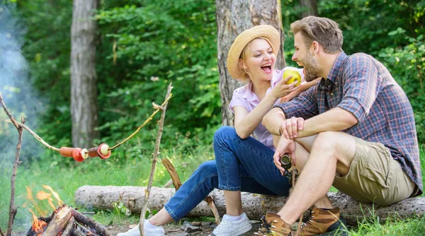 Have snack. Couple relaxing sit on log having snacks. Family enjoy romantic weekend in nature. Picnic roasting food over fire. Cooking at picnic. Girl offers eat apple while they waiting roasted food