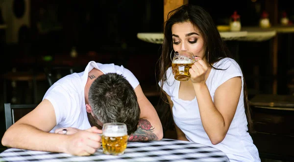 Enough for him. Couple in love on date drinks beer. Man drunk fall asleep on table and girl with full beer glass. She knows tricks how to drink and stay sober. Best friends or lover drink beer in pub