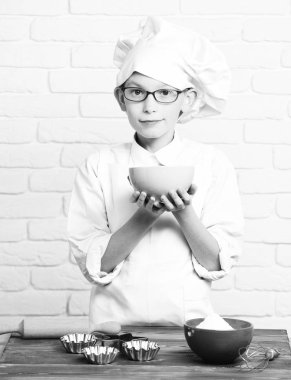 genç çocuk küçük sevimli aşçı Şef beyaz üniforma ve kek için tablo oklava kalıpları ile yakın duran ve turkuaz tutan gözlüklü güler yüz şapka tuğla duvar arka plan üzerinde kase