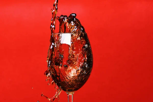 splash of drink in wine glass on red background, copy space.