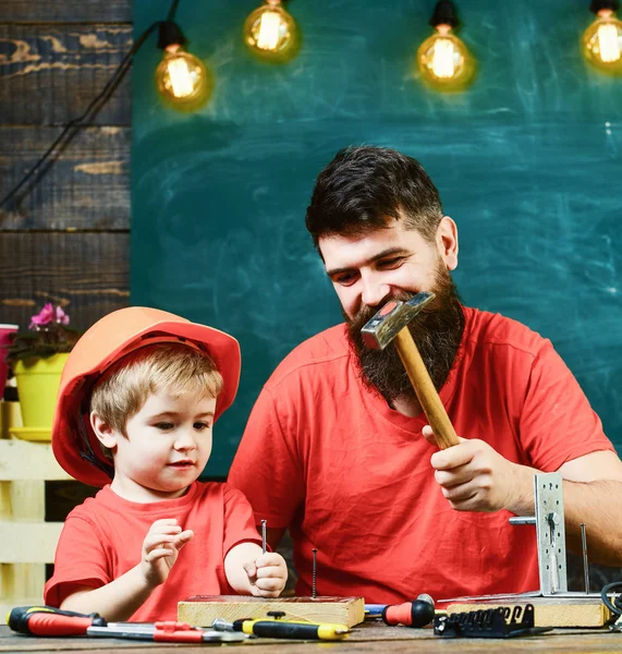 Niño, niño ocupado en casco protector hace a mano, reparación, trabajo con herramientas con papá. Concepto de trabajo en equipo. Padre con barba enseñando a su hijo a usar herramientas en el aula, pizarra en el fondo — Foto de Stock