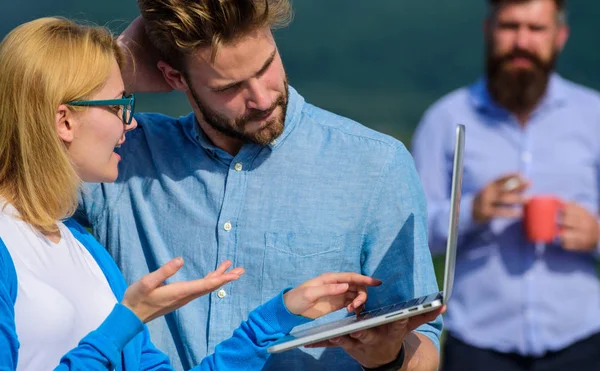 Couple works despite of coffee break. Colleagues with laptop work outdoor sunny day, nature background. Workaholics concept. Colleagues working laptop, boss smoking while coffee break on background