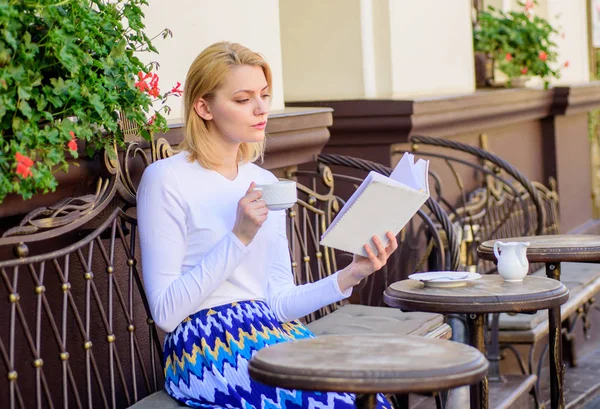 Lány Kávéznak, miközben olvasási bestseller könyv népszerű szerző. Olvasás a hobbija is. Bögre kávé és érdekes könyv kombináció tökéletes hétvégi. Nő kell inni kávézó terasz szabadban — Stock Fotó