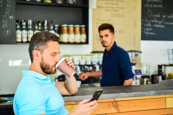 Have sip of energy. Man client with beard enjoy coffee in paper cup. Drinks to go useful option in modern cafe. Man holds paper cup with coffee barista guy stand on background. Client got his drink