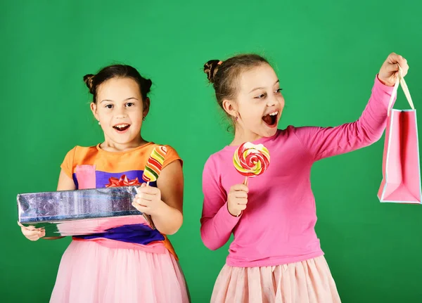 Hermanas con piruletas, cajas y bolsas. Los niños comen caramelos coloridos — Foto de Stock
