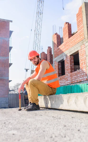 Gilet de construction et casque chantier de construction assis relaxant. Casque de protection homme assis devant le bâtiment en briques. Prenez le temps de vous détendre. Homme marteau prendre pause journée de travail sur le site de construction — Photo