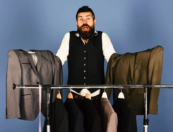 Designer makes choice near clothes hangers. Man with beard