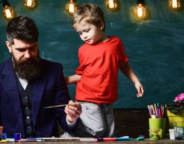 Sanat ders kavramı. Sakallı öğretmeni, sınıfta, kara tahta arka plan çizmek için küçük oğlu baba öğretir. Yetenekli sanatçı oğlu ile vakit geçirmek. Neşeli çocuk ve resim, çizim öğretmen